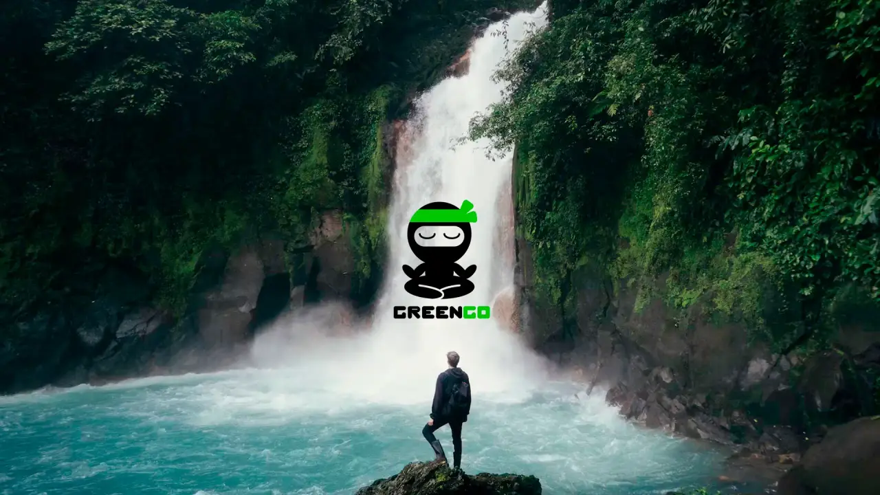 A beautiful waterfall with a man standing on a rock in front of it with a GreenGo logo in the center.