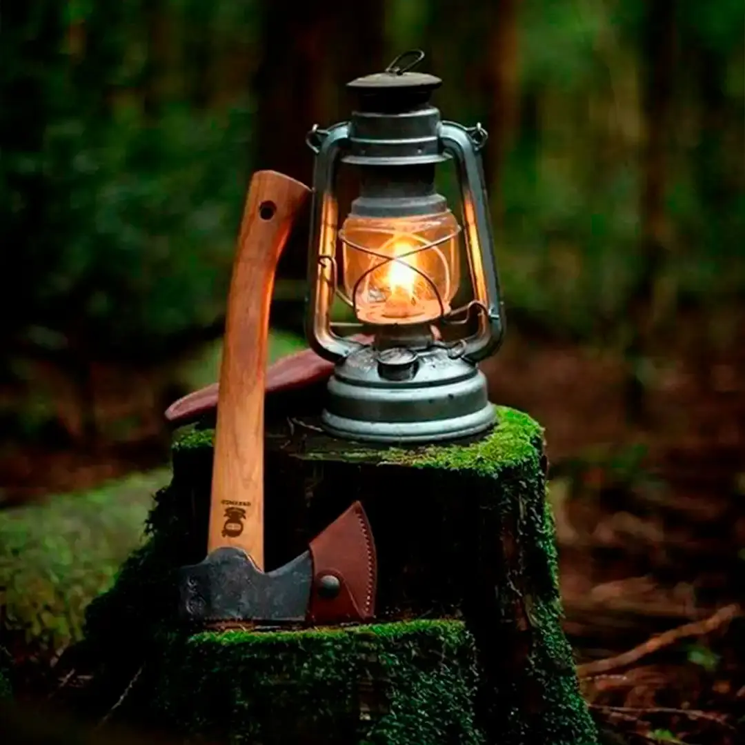 A GreenGo branded axe and a camping lantern placed on a mossy forest stump.