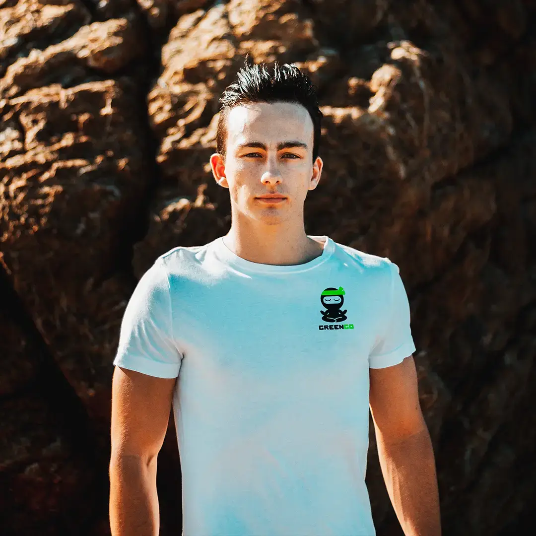 A man wearing a white branded with GreenGo logo shirt, standing in front of a big stone .