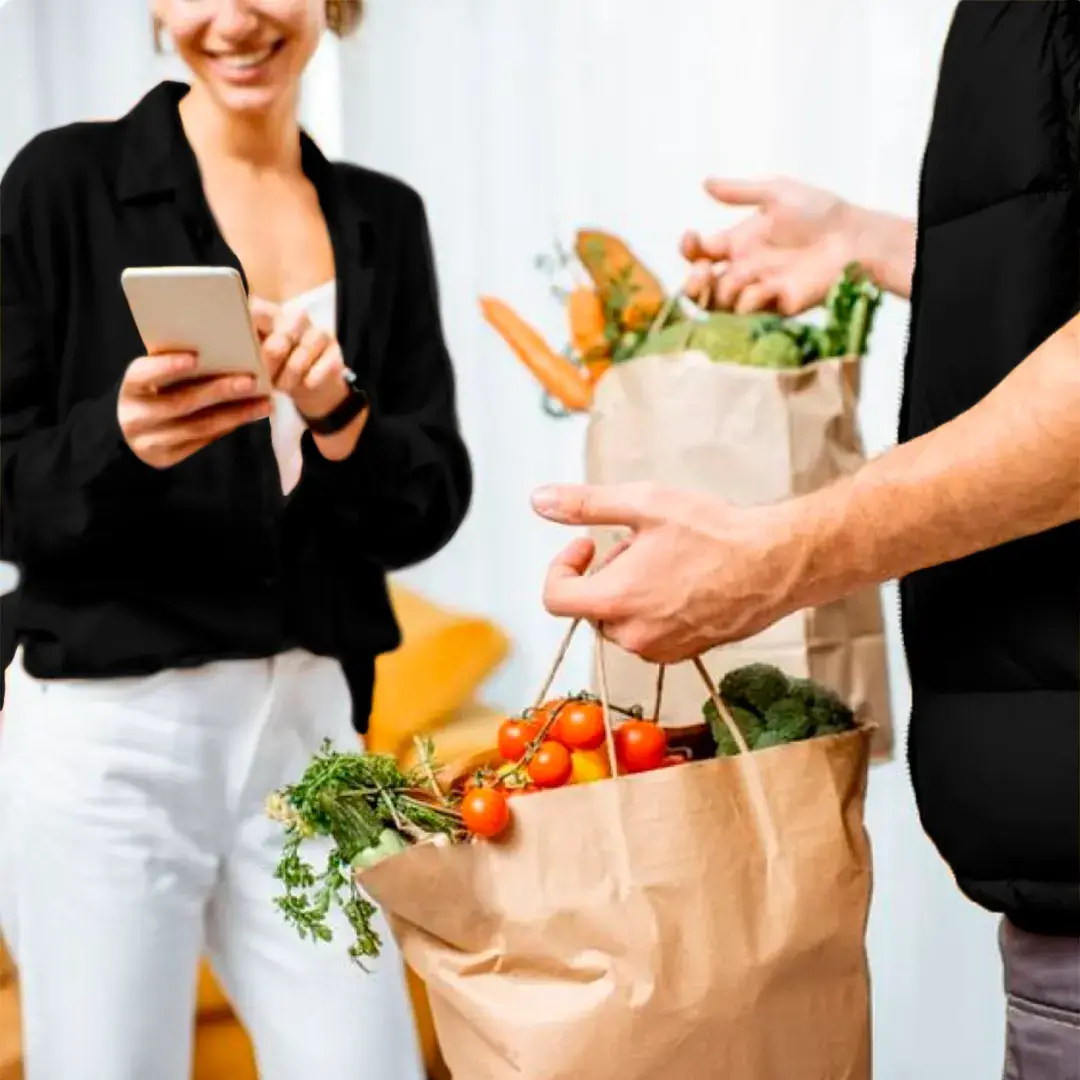 A couple of people wearing black and white clothes, shopping with paper bags full of vegetables.