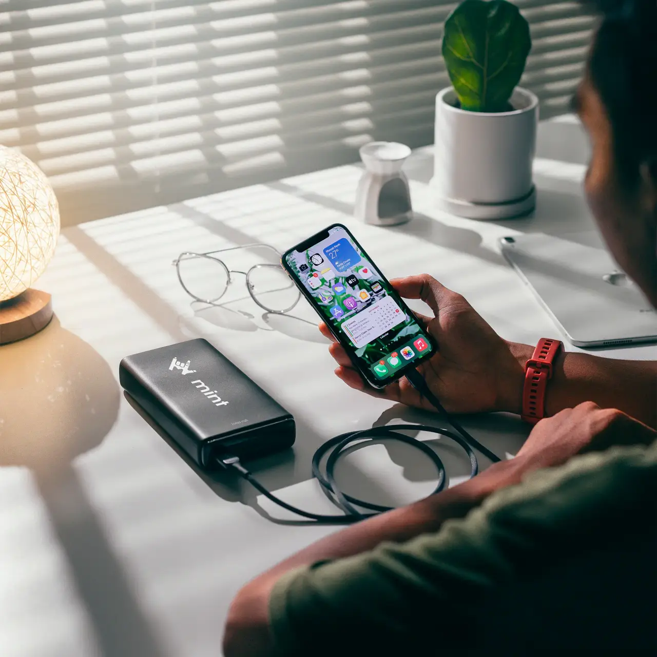 A photo of a man holding a phone that connected to a powerbank branded with Mint logo.